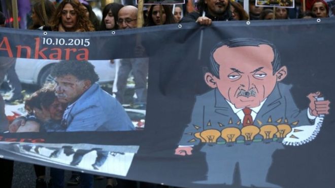 Демонстранты держат плакат с изображением президента Турции Тайипа Эрдогана (справа) и бомбардировками жертв во время марша в память жертв субботней бомбардировки в Анкаре (14 октября 2015 года)