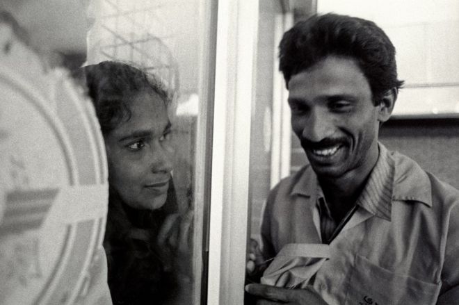 Женщина смотрит на мужа через окно в аэропорту Дакки