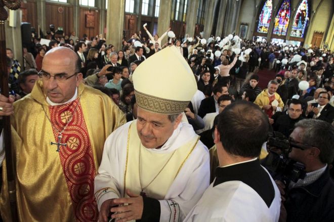 Епископ Хуан Баррос (С) посещает свою первую религиозную службу, когда люди протестуют против него в соборе Осорно, к югу от Сантьяго, Чили, 21 марта 2015 года