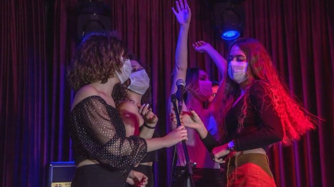 Grupos de chicas cantando con mascarillas en un club nocturno.