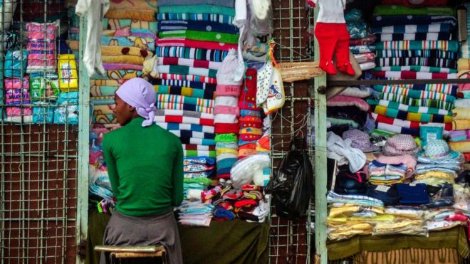 Продавец сидит в киоске, торгующем тканевыми полотенцами, шляпами и другим текстилем в столице Зимбабве Хараре 16 ноября 2017 года