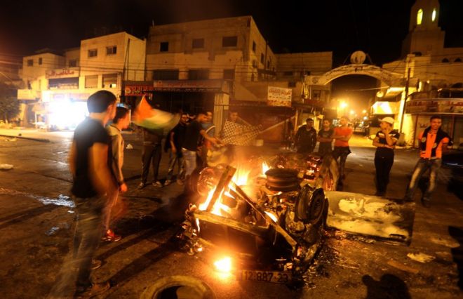 Палестинцы стоят возле горящего автомобиля, принадлежащего израильскому поселенцу, в городе Наблус на Западном берегу 18 октября 2015 года