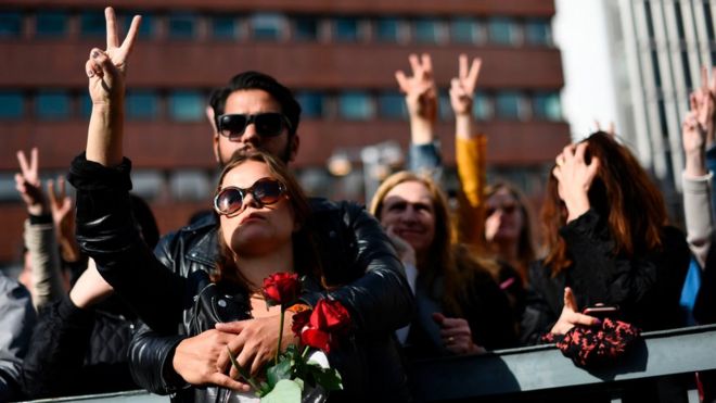 Люди высвечивают знак победы, когда они присутствуют на церемонии поминовения на площади Сергельс Торг в Стокгольме, Швеция, 9 апреля 2017 года