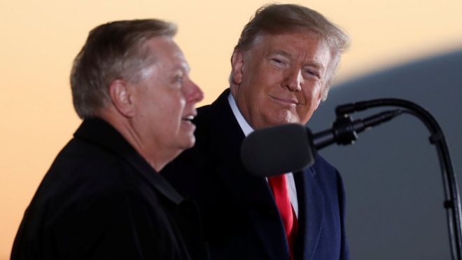 El presidente Donald Trump escucha a la senadora Lindsey Graham durante un mitin de campaña en Tupelo, Mississippi, el 26 de noviembre de 2018