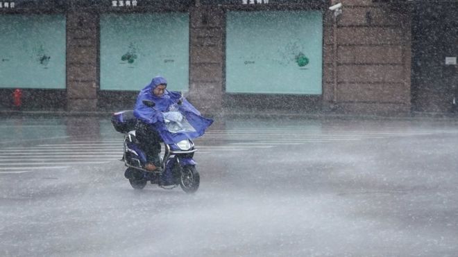 Мужчина едет на электросамокате во время ливня, когда приближается тайфун Лекима в Шанхае, Китай