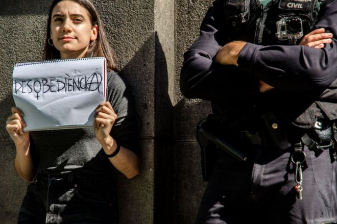 Mujer joven con un cuaderno en el que escribió "desobediencia" junto a un guardia civil el 20 de septiembre en Barcelona.