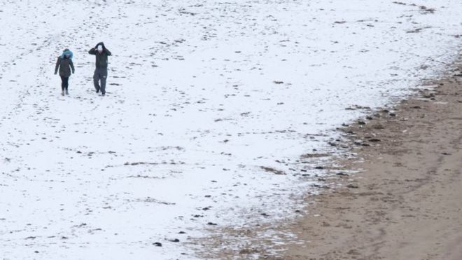 Пара гуляет по снегу вдоль пляжа на морском курорте Скарборо в Северном Йоркшире