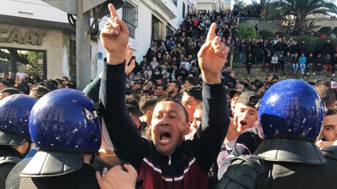 A man gestures as he is surrounded by police during protests in Algeria