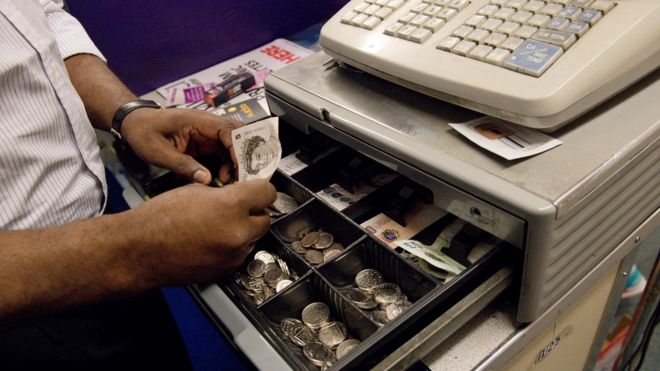 Работник берет оплату за товары и кладет деньги в кассу, содержащую несколько монет достоинством в фунты, и купюры в магазине в Лондоне 7 октября 2016 года.