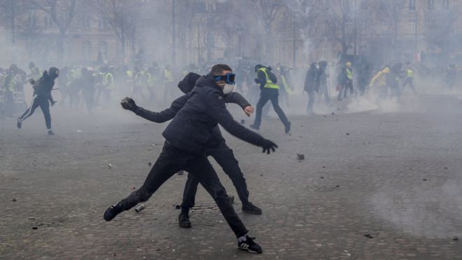 Демонстранты бросают булыжники в силы ОМОНа во время столкновений возле Триумфальной арки в Париже 16 марта 2019 года.