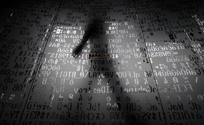 Силуэт человека, идущего за стеклянной стеной с символами машинного кодирования в штаб-квартире гиганта интернет-безопасности «Касперский» в Москве