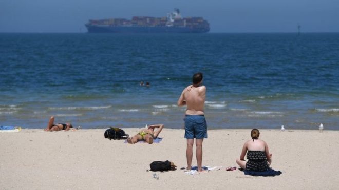 Beachgoers apply sunscreen on a hot day in Melbourne