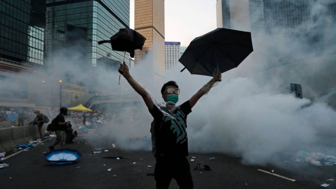 Протестующий (С) поднимает свои зонтики перед слезоточивым газом, который был запущен ОМОНом для разгона демонстрантов, блокирующих главную улицу к финансовому Центральному району за пределами правительственного штаба в Гонконге, 28 сентября 2014 года.