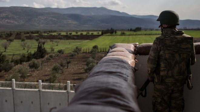 Турецкий солдат смотрит через границу на стену в Сирию