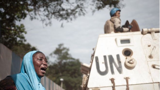 Женщина реагирует рядом с солдатами ООН, когда 11 апреля 2018 года жители штаб-квартиры МИНУСКА, миротворческая миссия ООН в Центральноафриканской Республике, в Банги, проводят демонстрации у жителей мусульманского района PK5. Войска ООН и рабочие Красного Креста вывезли трупы, оставленные демонстрантами