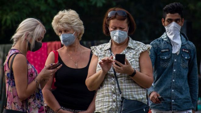 Un grupo de personas con mascarillas mirando sus celulares