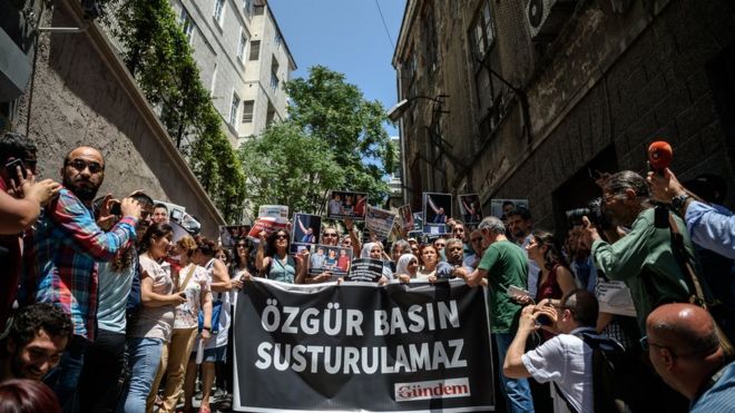 Протестующие держат фотографии заключенного в тюрьму активиста RWB Эрол Ондероглу, журналиста Ахмета Несина и активиста и ученого Себнема Корура Финканчи с плакатом с надписью «свободная пресса не будет замолчать» перед штаб-квартирой прокурдской газеты Ozgur Gundem в Стамбуле 21 января 16 июня