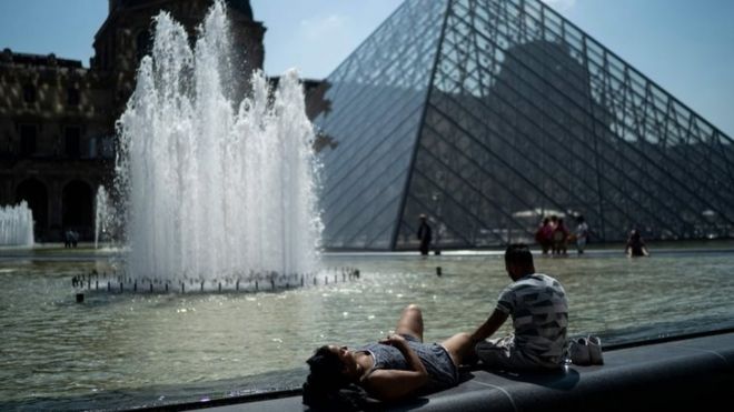People sunbath in front of the Louvre Pyramid (Pyramide du Louvre) during a heatwave in Paris