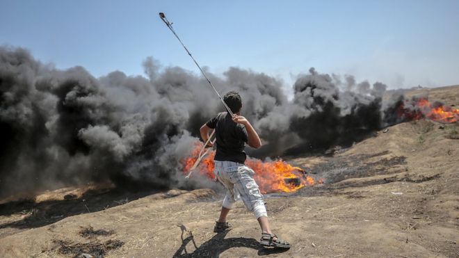 Палестинский протестующий бросает камни во время столкновений после акций протеста у границы с Израилем на востоке сектора Газа, 14 мая 2018 г. (