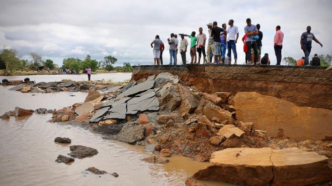 Местные жители стоят возле поврежденного участка дороги между Бейрой и Шимойо в районе Нхаматанда, центральный Мозамбик
