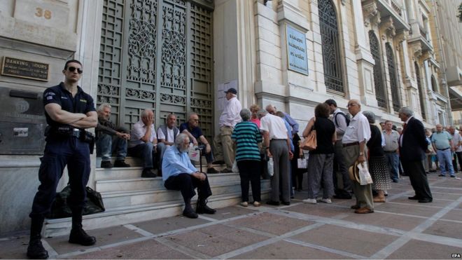 Полицейский стоит на страже, поскольку греческие пенсионеры выстраиваются в очередь, чтобы получить часть своих пенсий перед отделением Национального банка Греции в Афинах, Греция (9 июля 2015 года)