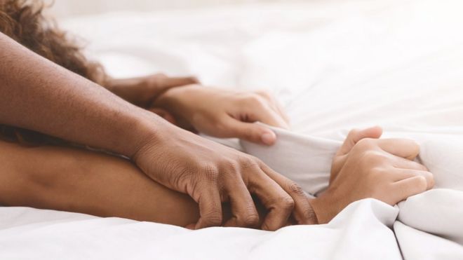 Los brazos entrelazados de un hombre y una mujer en una cama