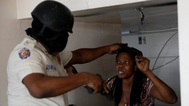 A Haitian National Police officer holds a woman found inside a bank office at a commercial area that was looted during protests against fuel price increases in Port-au-Prince, Haiti, July 8, 2018
