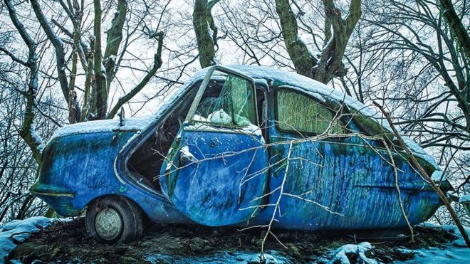 An abandoned blue car in an icy forest