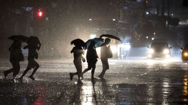 Люди используют зонтики, когда пересекают улицу во время сильного ливня в Маниле