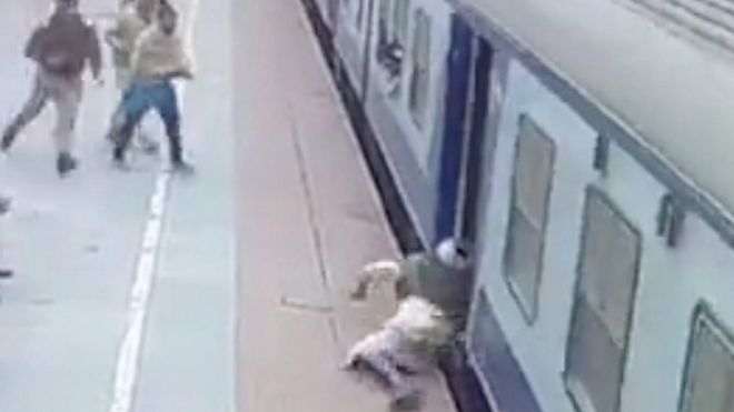 Man being dragged on station platform by moving train