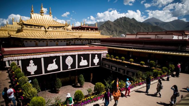 Китайские туристы на крыше храма Джокханг в Лхасе, на фоне которых видны горы