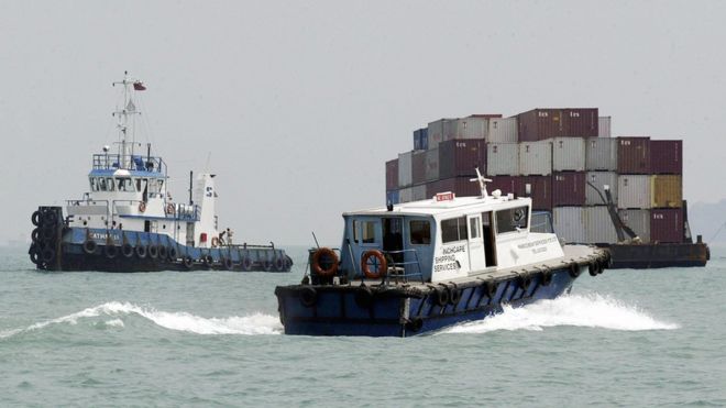 A shipping services boat passes a barge in Singapore