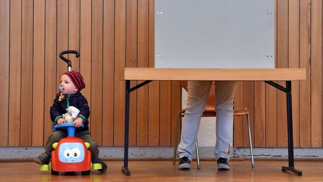 Ребенок смотрит, как избиратели заполняют избирательные бюллетени во время государственных выборов в Гессене (Hessen) на избирательном участке в Гинсхайме-Густавсбурге, центральная Германия