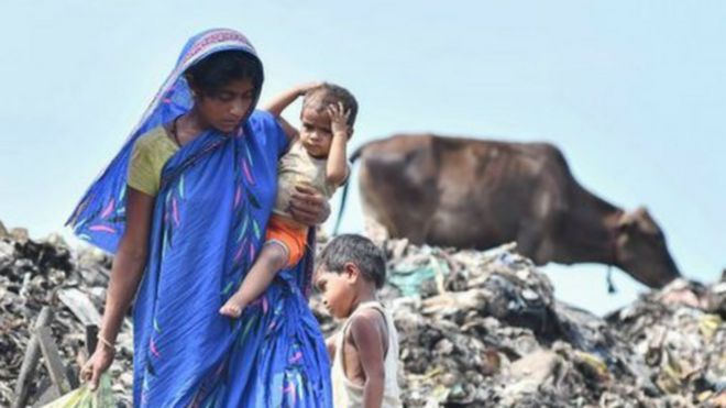 Una mujer de India carga a su bebé en brazos en un basurero.