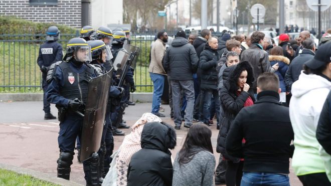 Французские сотрудники ОМОНа (слева) стоят на страже, когда люди собираются во время акции протеста 6 февраля 2017 года в Ольне-су-Буа, северный Париж