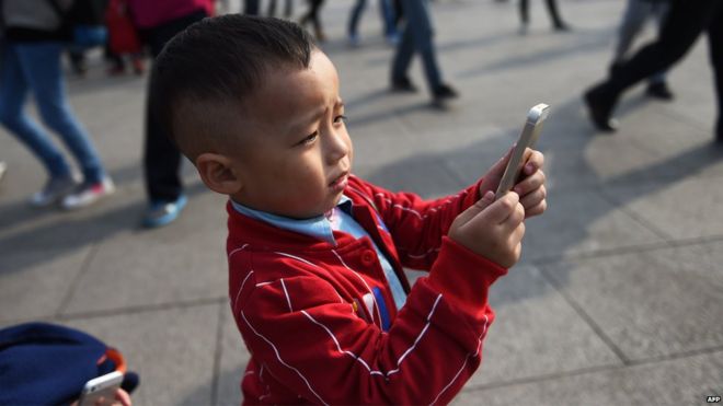 Молодой мальчик использует iPhone для фотографирования на площади Тяньаньмэнь в Пекине 30 сентября 2014 года