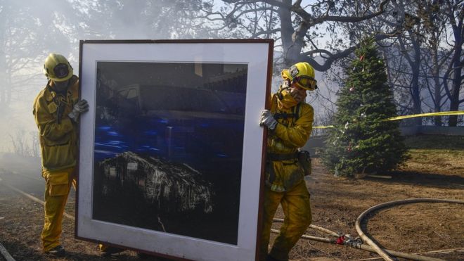 Firefighters remove a painting as they continue to extinguish fires in a home during the "Skirball Fire"