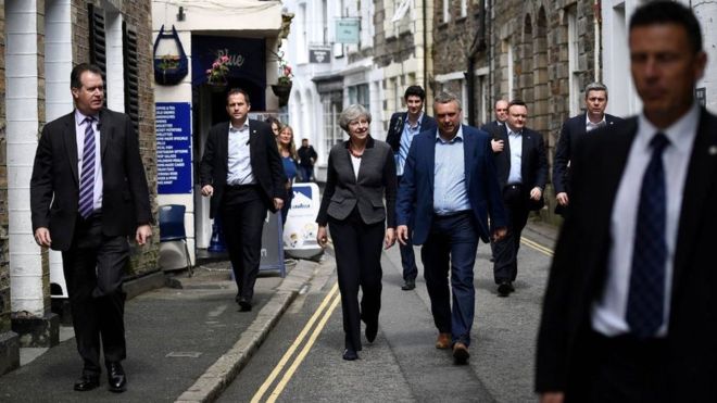 Премьер-министр Великобритании Тереза ​​Мэй (С) в окружении охранников, когда она идет по Мевагиссе, на юго-западе Англии, во время предвыборной кампании 2017 года