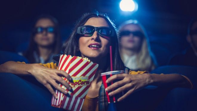 Женщина в кино с напитком и попкорном