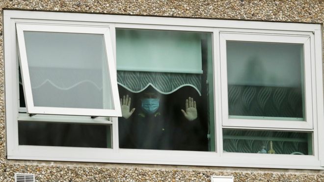 A man wearing a mask holds his hands up to the window in one of the housing towers