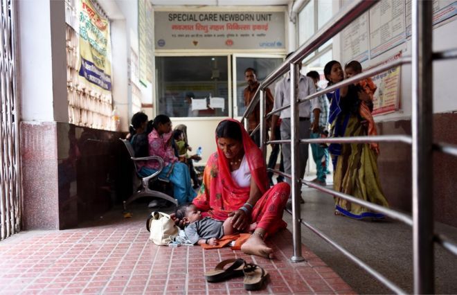 Индийская женщина сидит со своим ребенком в коридоре возле отделения по уходу за новорожденными в государственной больнице