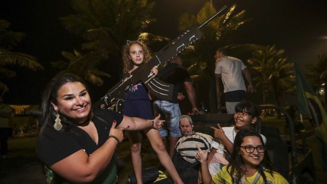 Девушка снимает фотографию с пистолетом из бумаги, когда сторонники крайне правого кандидата в президенты Бразилии Джейра Болсонаро празднуют его победу