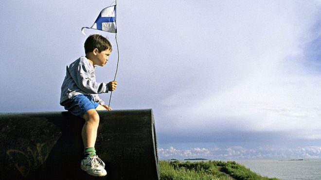 Niño con bandera de Finlandia sentado en un cañon