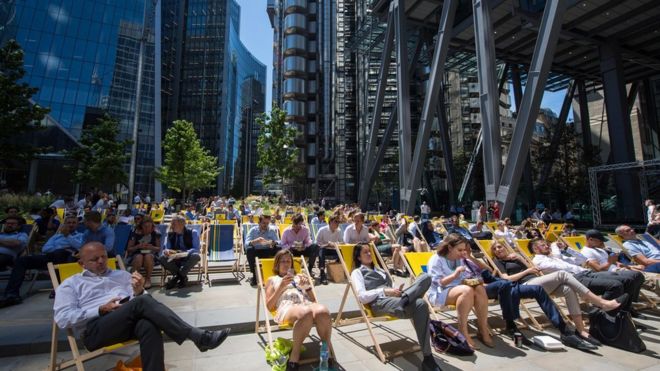 Люди наслаждаются обеденным перерывом на солнце в финансовом районе Лондона Сити