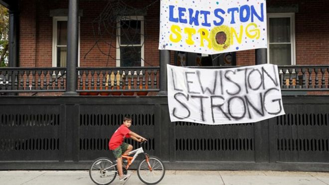A boy cycles past "Lewiston strong" banners
