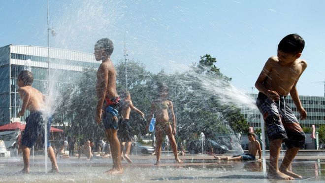 أطفال يلعبون بمضخات المياه في نافورة بقصر الأمم، خلال موجة الحر، في جنيف بسويسرا