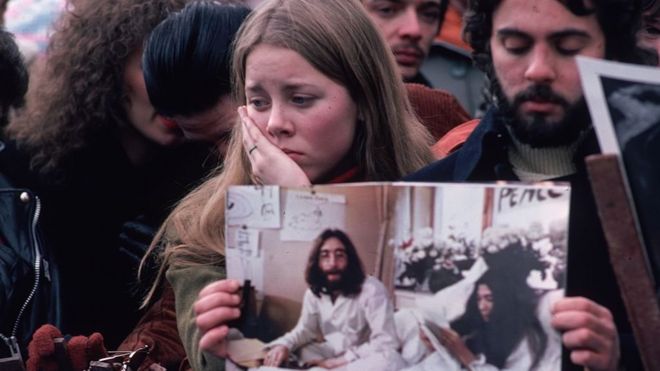 Jóvenes apesumbrados con una foto de John Lennon, lamentando su muerte