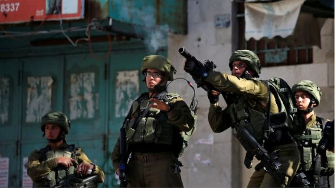 Израильский солдат стреляет слезоточивым газом в сторону палестинцев во время столкновений в Хевроне (12/04/19)
