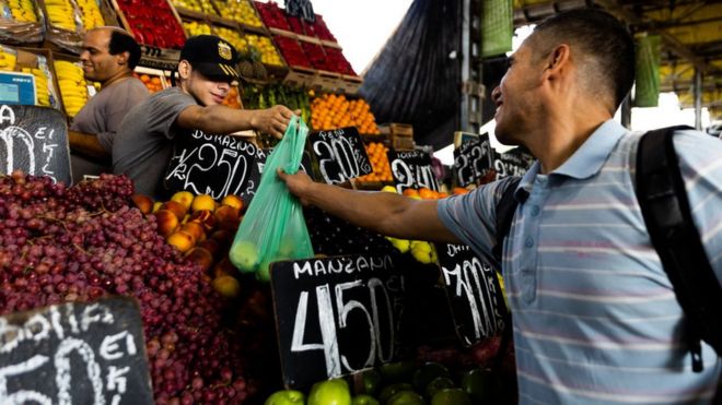 Un comerciante entrega una bolsa con alimentos a un consumidor