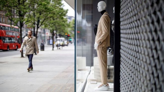 A man walks past the window display of a clothing store, closed-down due to the coronavirus lockdown